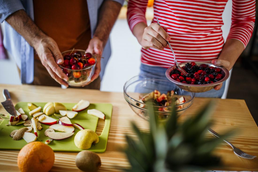 People making a fruit salad in kitchen using berries and apples for whole30 diet