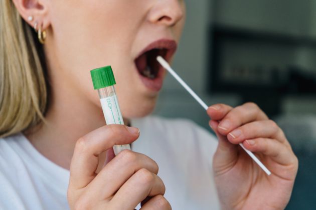 Young woman holds a swab into her mouth and holding a medical tube for the coronavirus / covid19 home