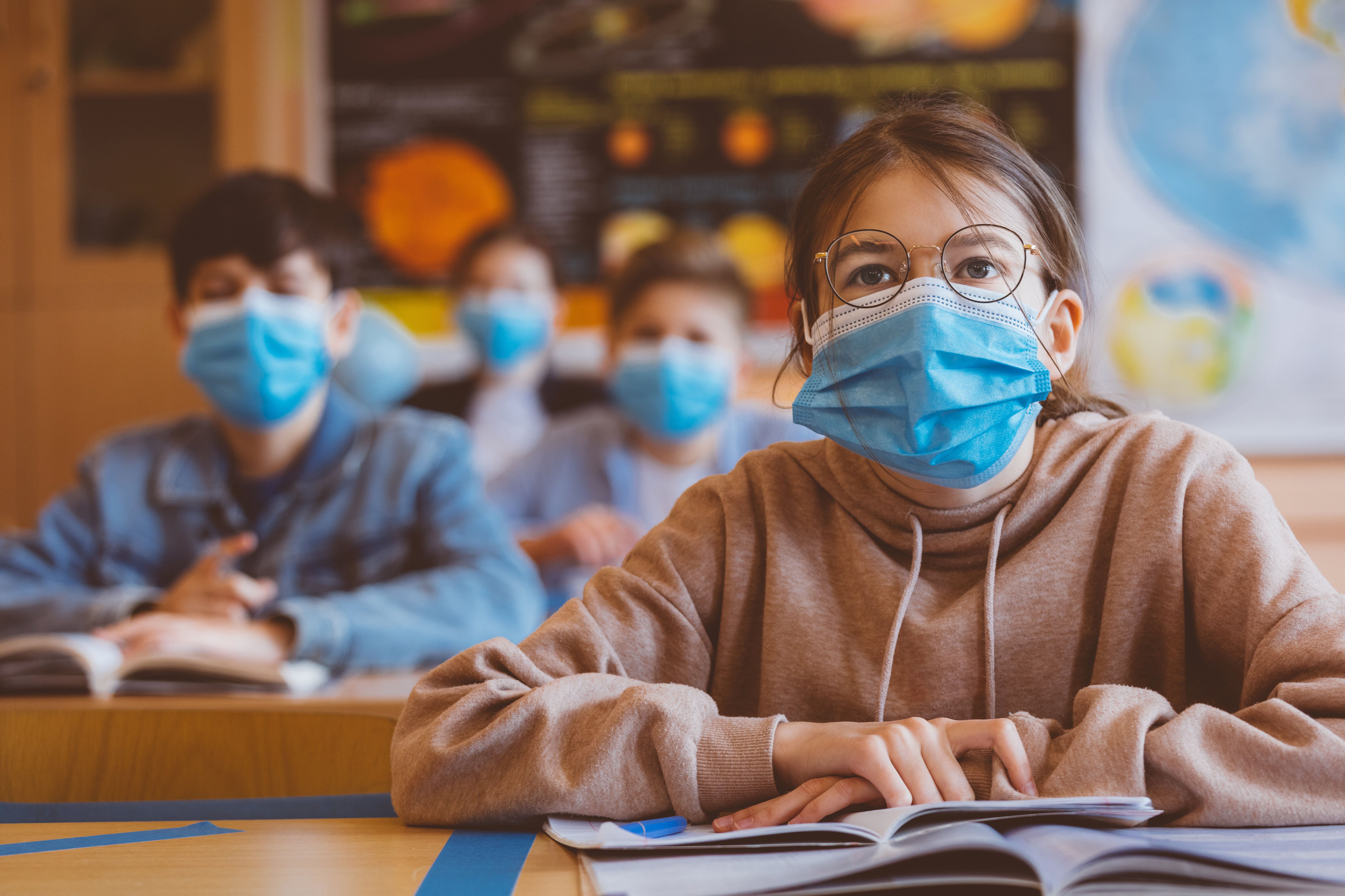 High school students at school, wearing N95 Face masks. Teenage girl wearing eyeglasses sitting at the...