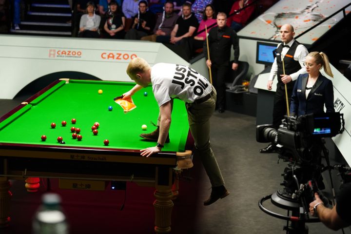 A Just Stop Oil protester jumps on the table and throws orange powder during the match between Robert Milkins against Joe Perry during day three of the Cazoo World Snooker Championship at the Crucible Theatre, Sheffield. Picture date: Monday April 17, 2023. (Photo by Mike Egerton/PA Images via Getty Images)